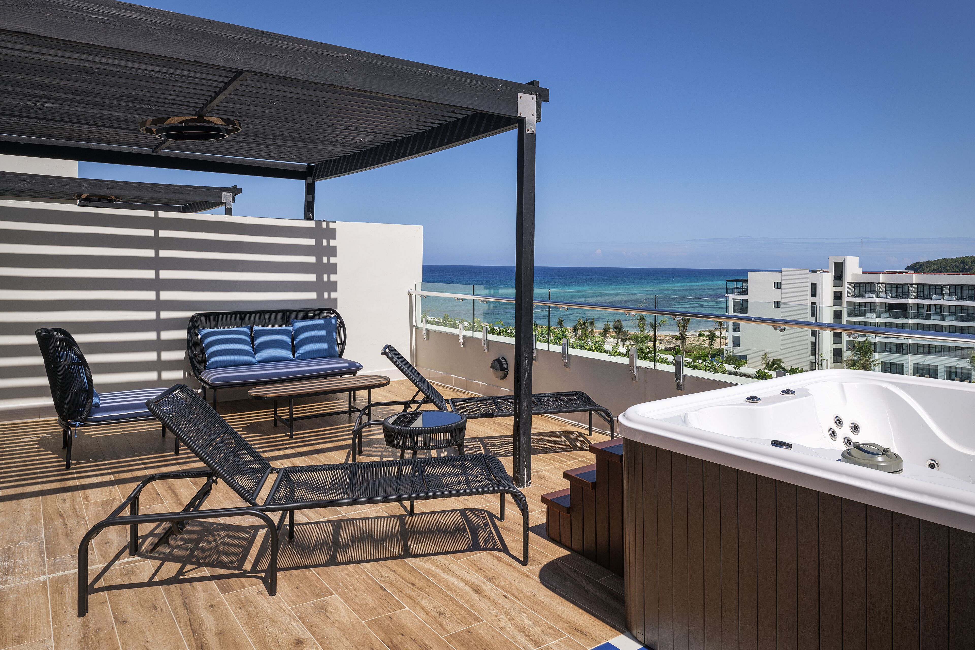 A balcony with a hot tub, lounge chairs, and a view of the ocean.