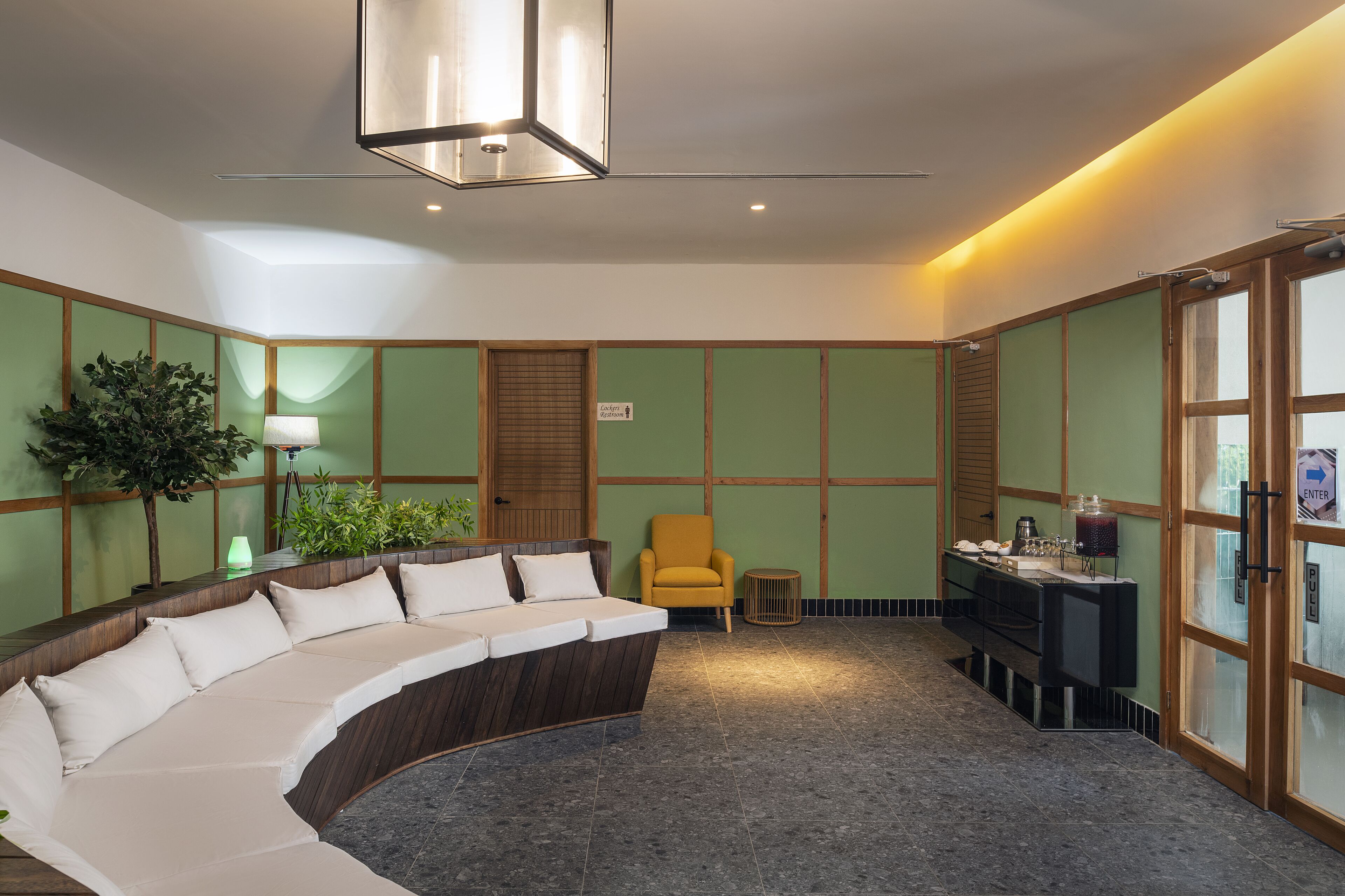 A modern hotel lobby with a curved sofa, a yellow armchair, a small table with a lamp, and a reception desk.