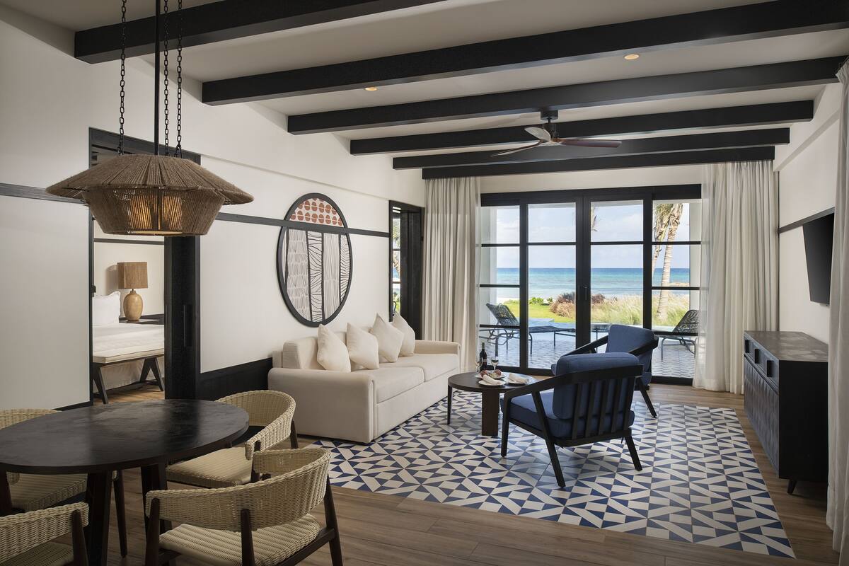 A modern living room with a sofa, chairs, a dining table, and a view of the ocean.