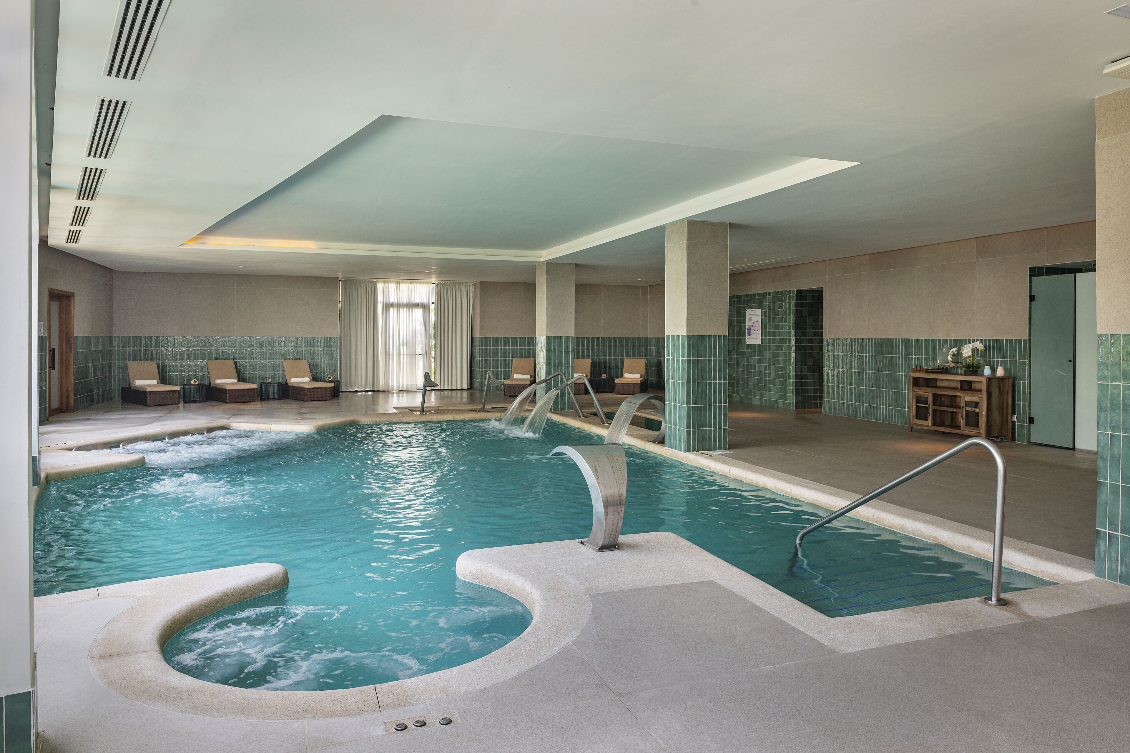 A swimming pool with a hot tub, lounge chairs, and a tiled wall.
