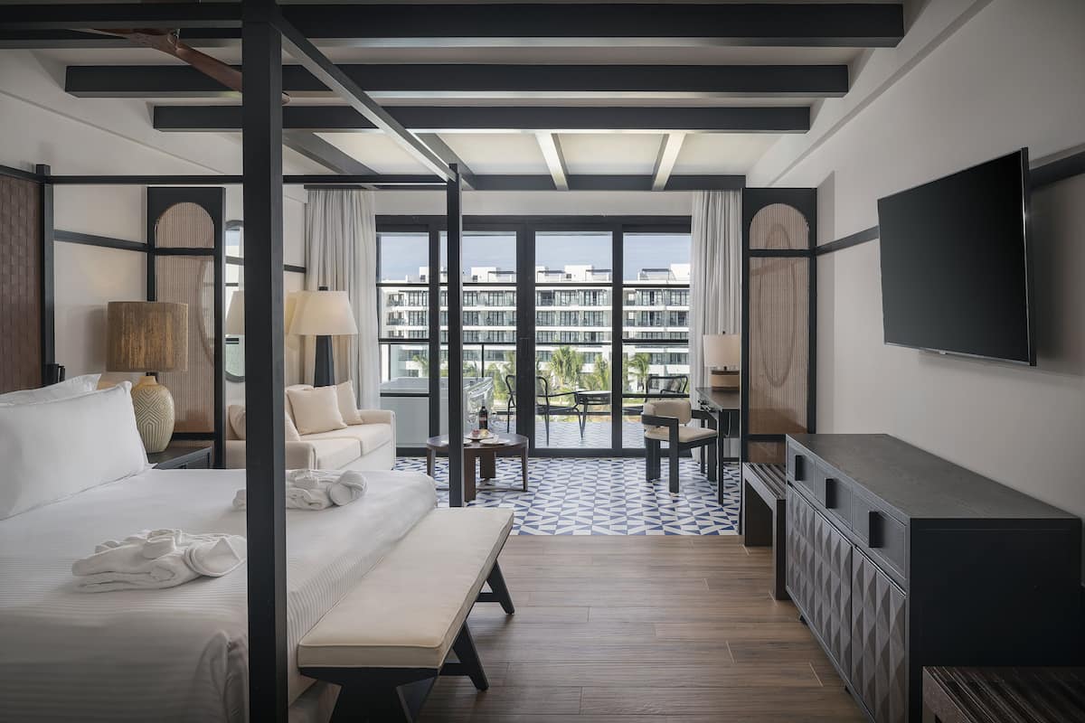 A modern hotel room with a large bed, a desk, a TV, and a balcony with a view of the city.