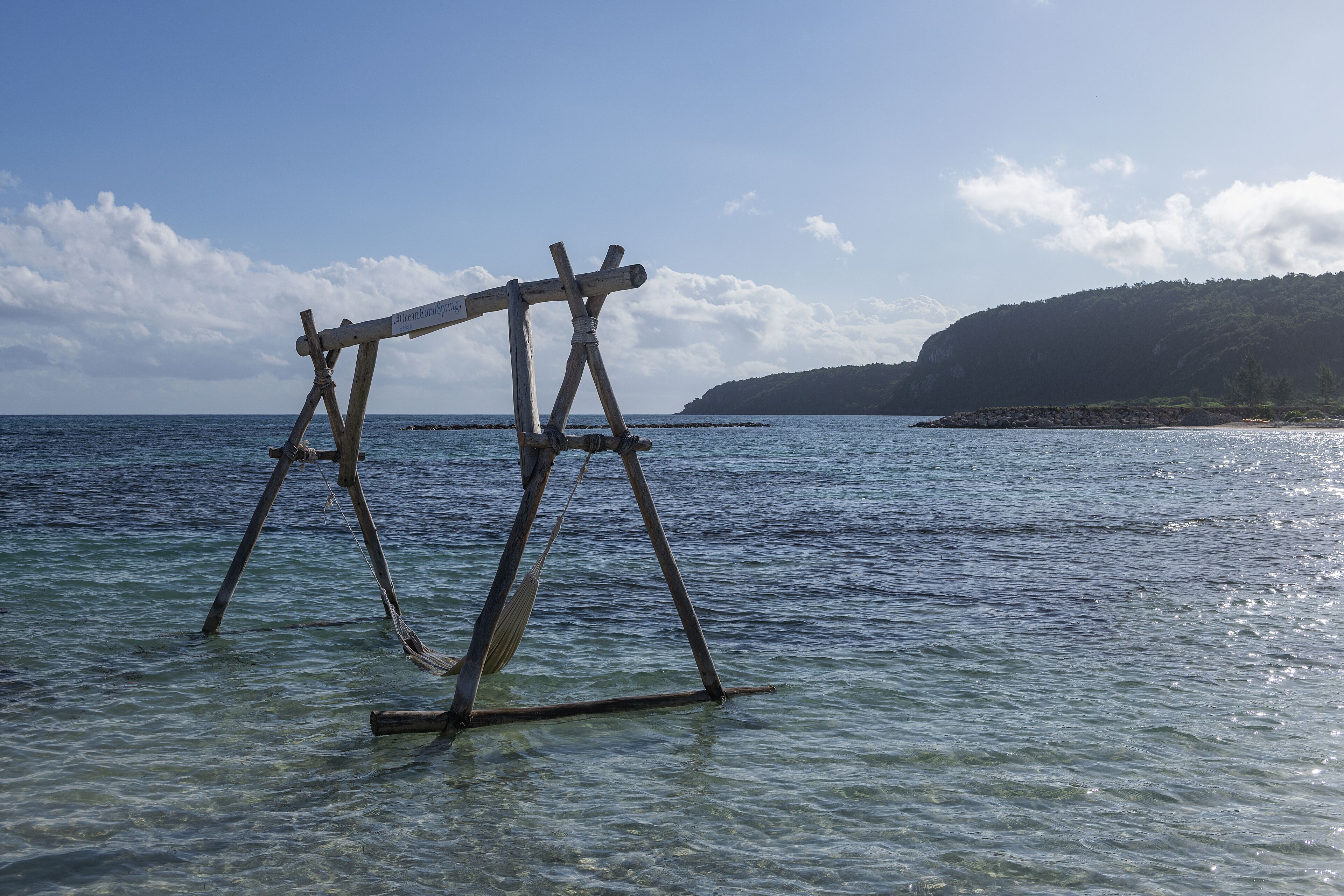 Une balançoire en bois suspendue au-dessus d’une eau claire, avec une chaîne de montagnes en arrière-plan.