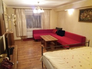 Une pièce avec un canapé rouge, une table en bois, un lit, une fenêtre avec des rideaux et un lustre.