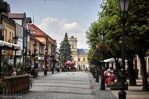 Une rue pavée bordée d’immeubles, avec des terrasses et une tour de l’horloge en arrière-plan.