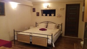 A bedroom with a metal bed frame, a wooden floor, a red bench, a wall-mounted shelf with decorative items, and a door.