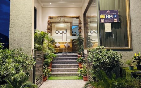 A hotel entrance with a staircase leading to a reception area. There are potted plants on either side of the entrance, and a sign on the right wall.