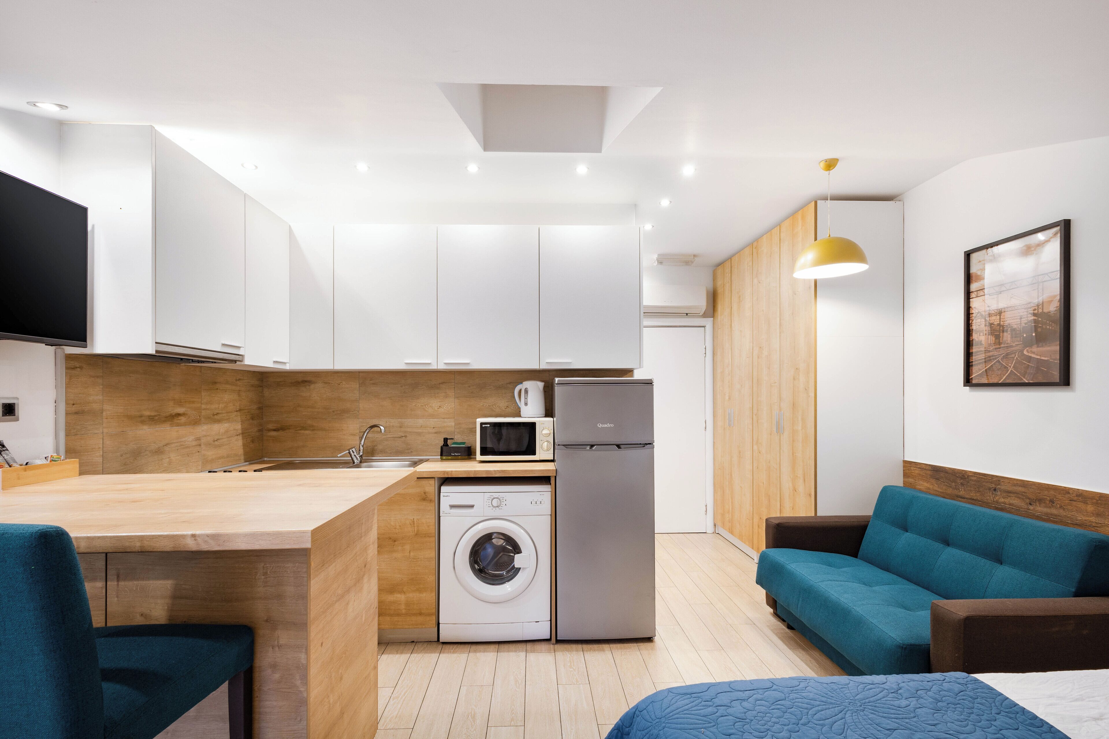 Un espacio habitable compacto con kitchenette, lavadora, refrigerador, sofá y cama.