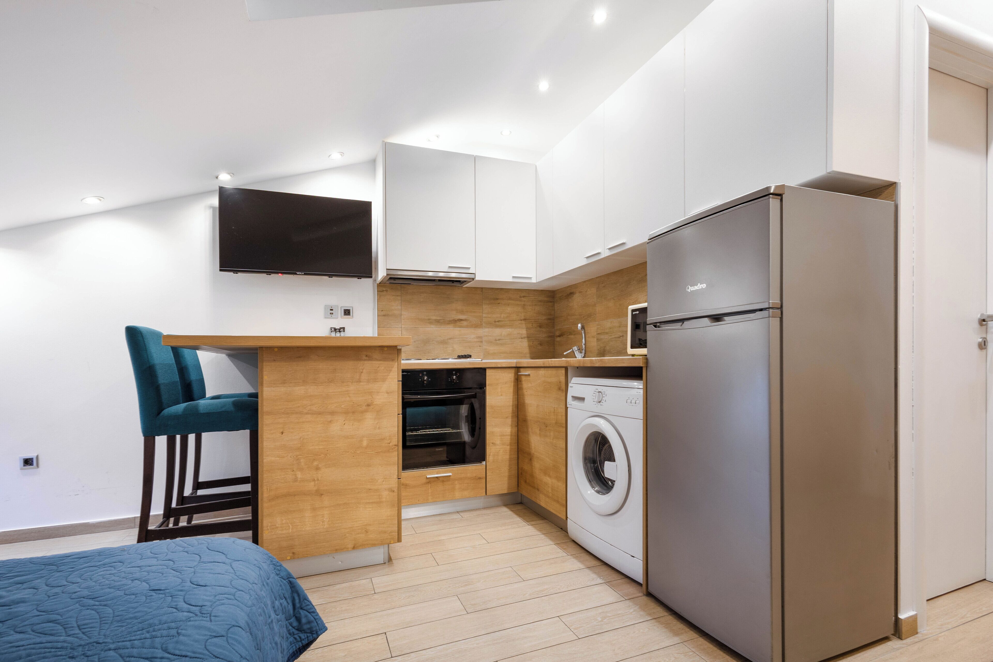 A compact kitchen with a washing machine, a built-in oven, and a flat-screen TV.