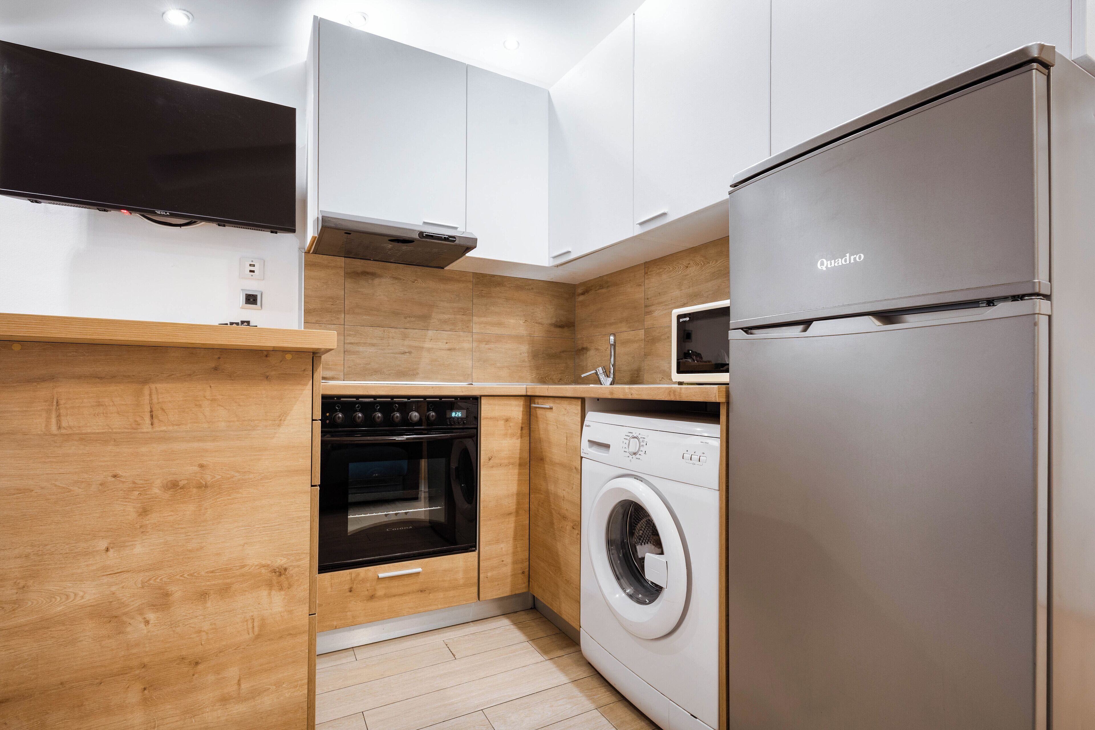 Cucina moderna con mobili in legno, forno integrato, lavatrice e frigorifero in acciaio inossidabile.