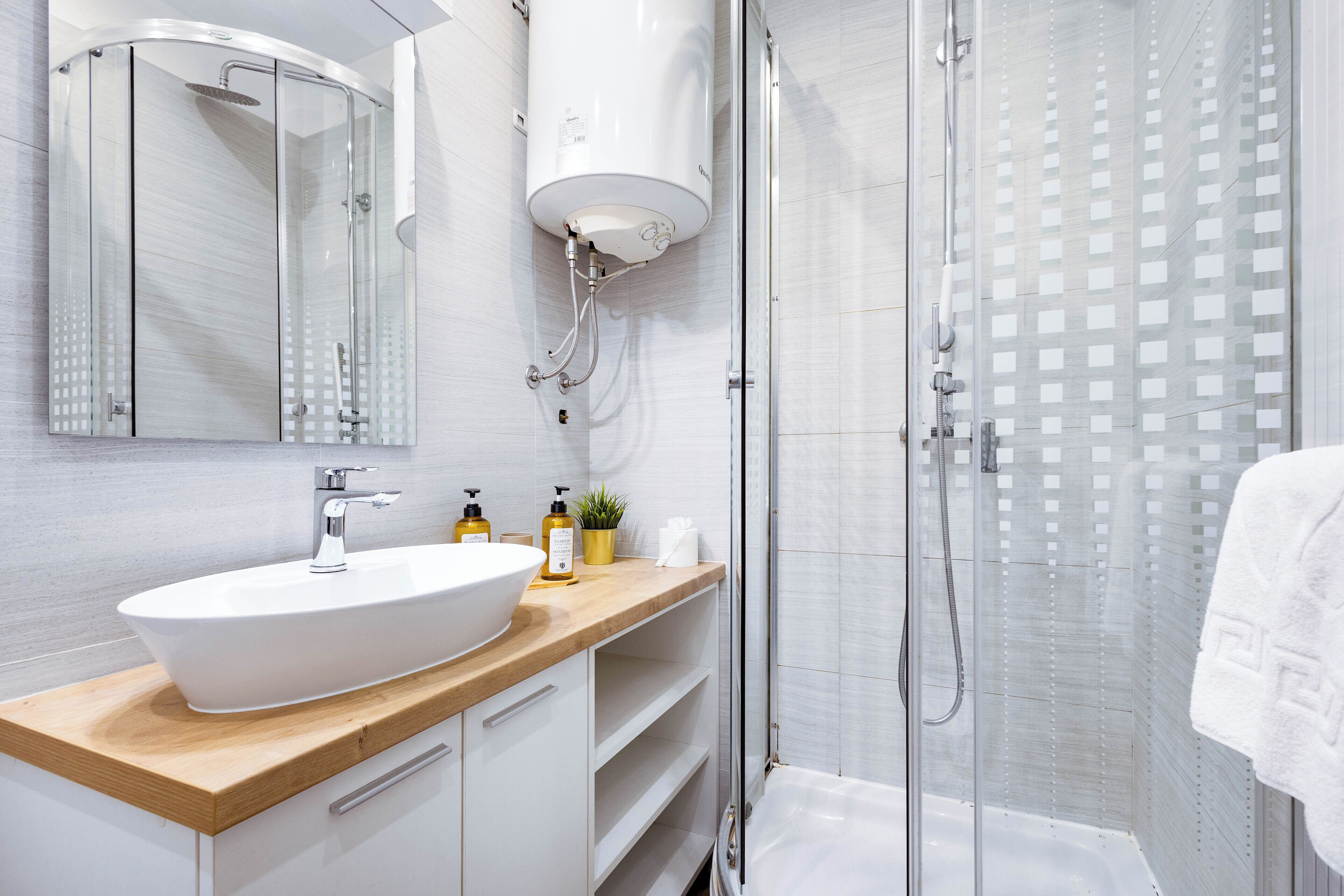 A modern bathroom with a large white sink, a wooden countertop, a glass shower enclosure, and a towel hanging on the wall.