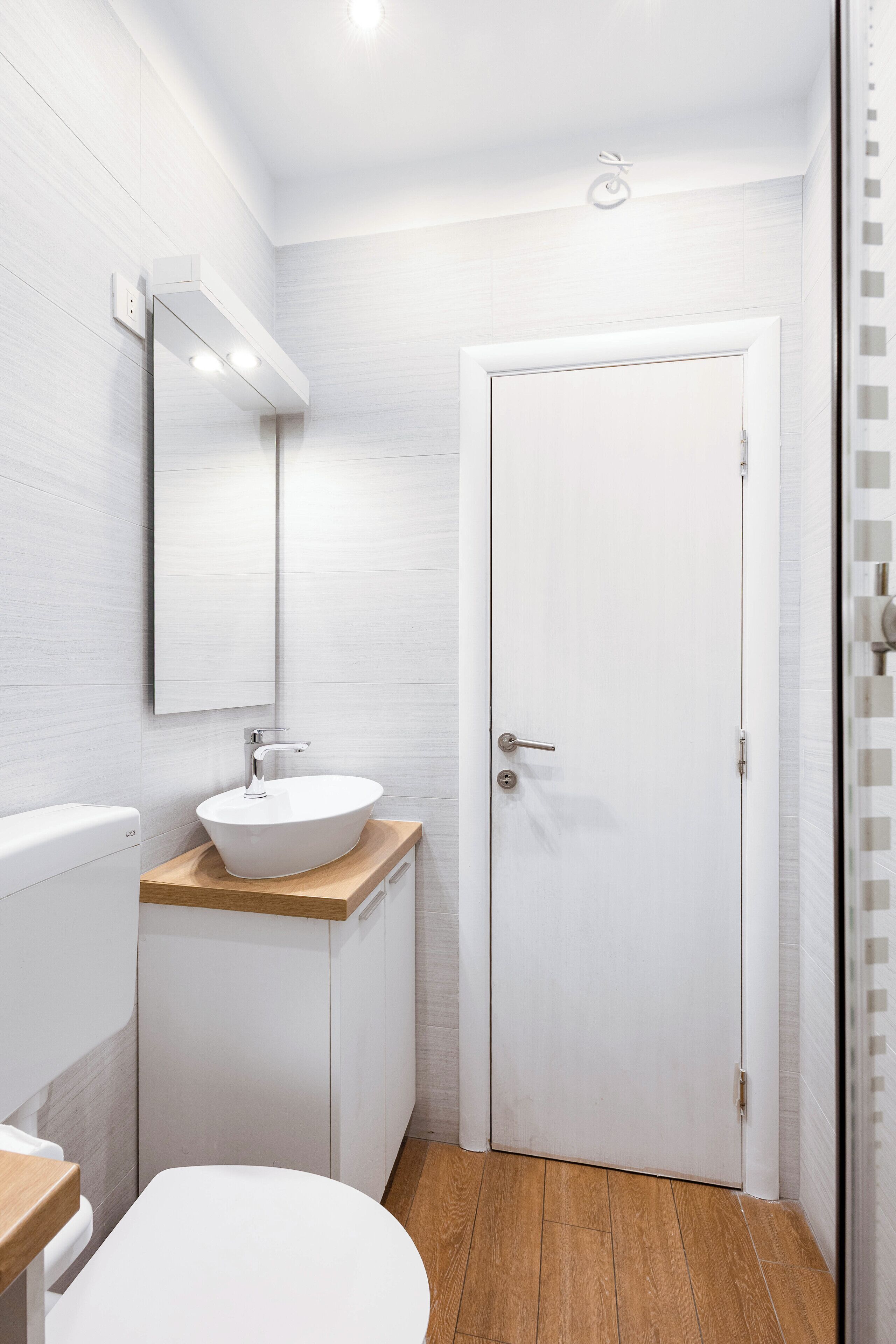 A modern bathroom with a white sink, wooden countertop, and a white door.