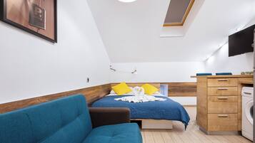 Ett litet sovrum med en säng, en soffa, ett träskåp och en tvättmaskin.