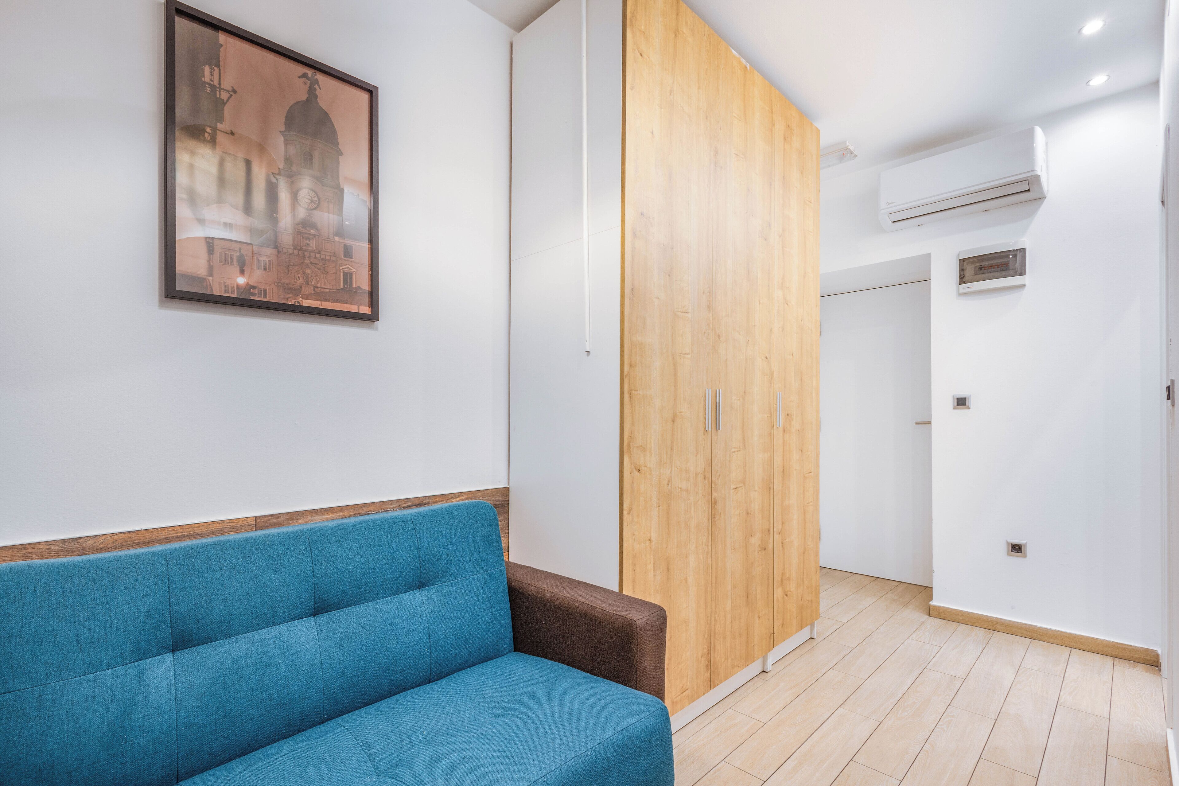 Una habitación moderna con un sofá azul, un armario de madera y un equipo de aire acondicionado en la pared.