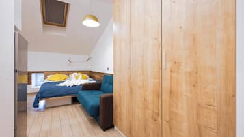 A bedroom with a bed, a blue sofa, wooden wardrobe, and a skylight.