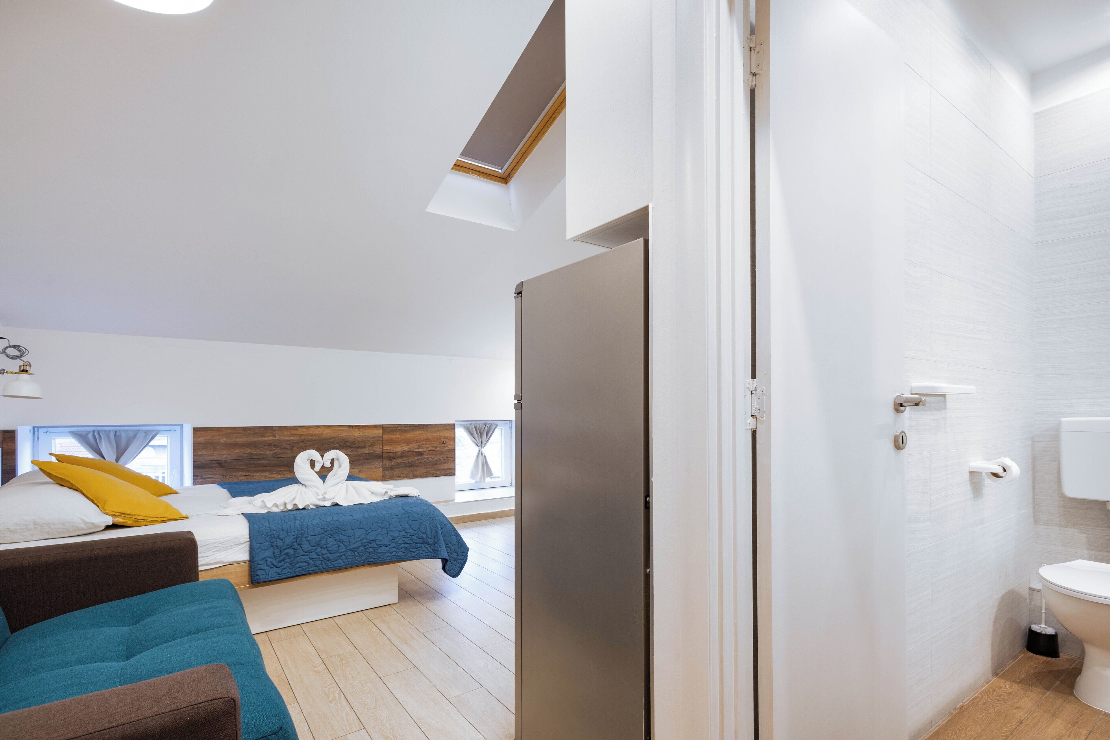 Un dormitorio moderno con cama, sofá, tragaluz y baño con inodoro y lavamanos.