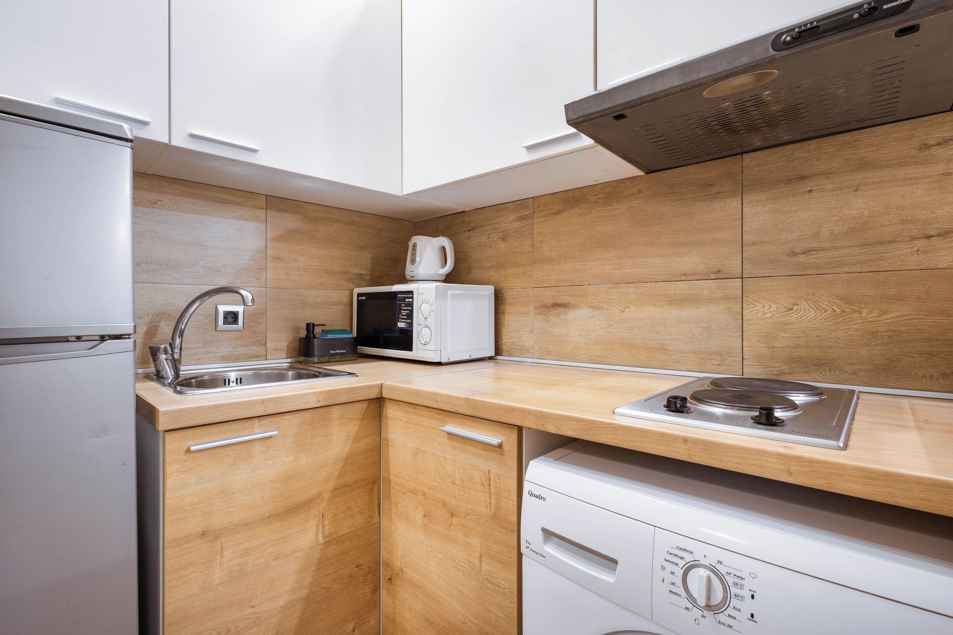A compact kitchen with white cabinets, a microwave, a coffee maker, a sink, and a dishwasher.