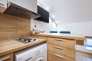 A compact kitchen with wooden cabinetry, a built-in washing machine, and a flat-screen TV mounted on the wall. - Apartments Pomerio Rijeka (Rijeka)