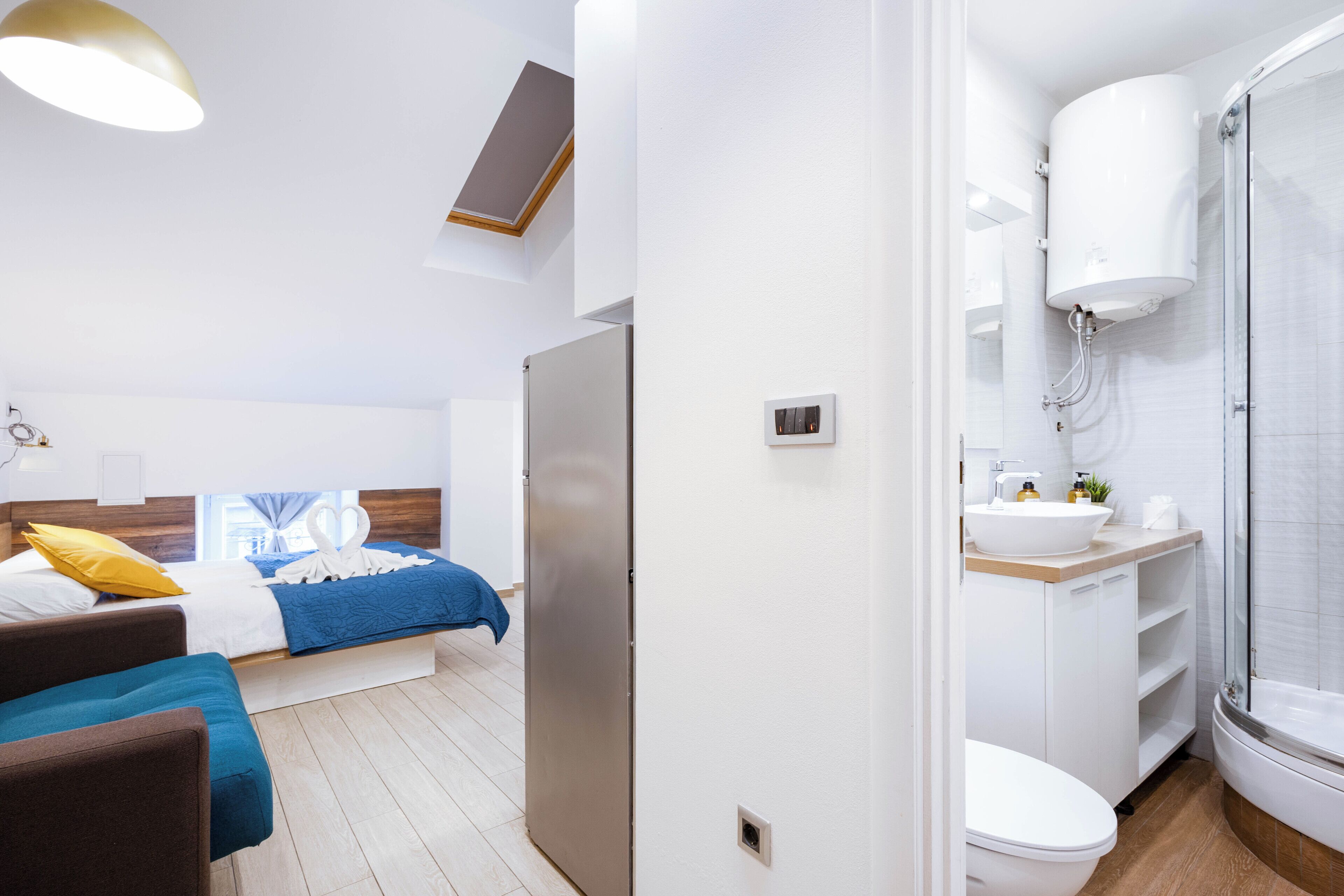 A modern hotel room with a bed, a sofa, a bathroom with a shower, and a toilet.