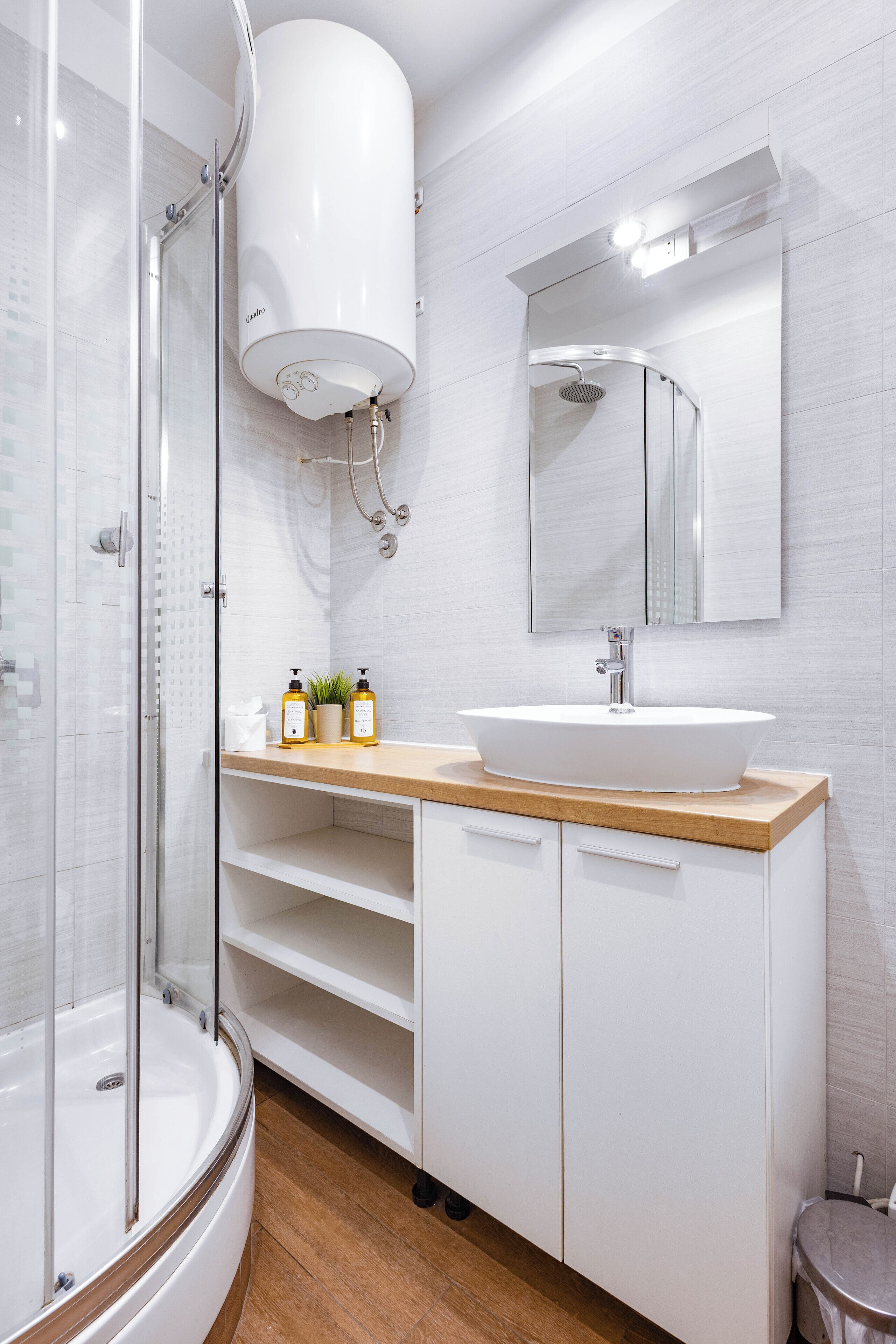 A modern bathroom with a glass-enclosed shower, a white sink with a wooden countertop, and a large mirror above the sink.