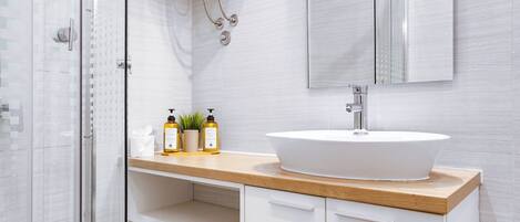 Une salle de bain moderne avec une douche à parois de verre, un lavabo blanc doté d’un plan de travail en bois et un grand miroir au-dessus du lavabo.