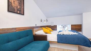 A modern bedroom with a wooden headboard, a bed with a blue quilt, a teal sofa, and a framed picture on the wall.