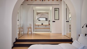 A modern bedroom with a wooden floor, white bed, and a large mirror. - Belvedere Hotel - The Leading Hotels of the World  (Mykonos)