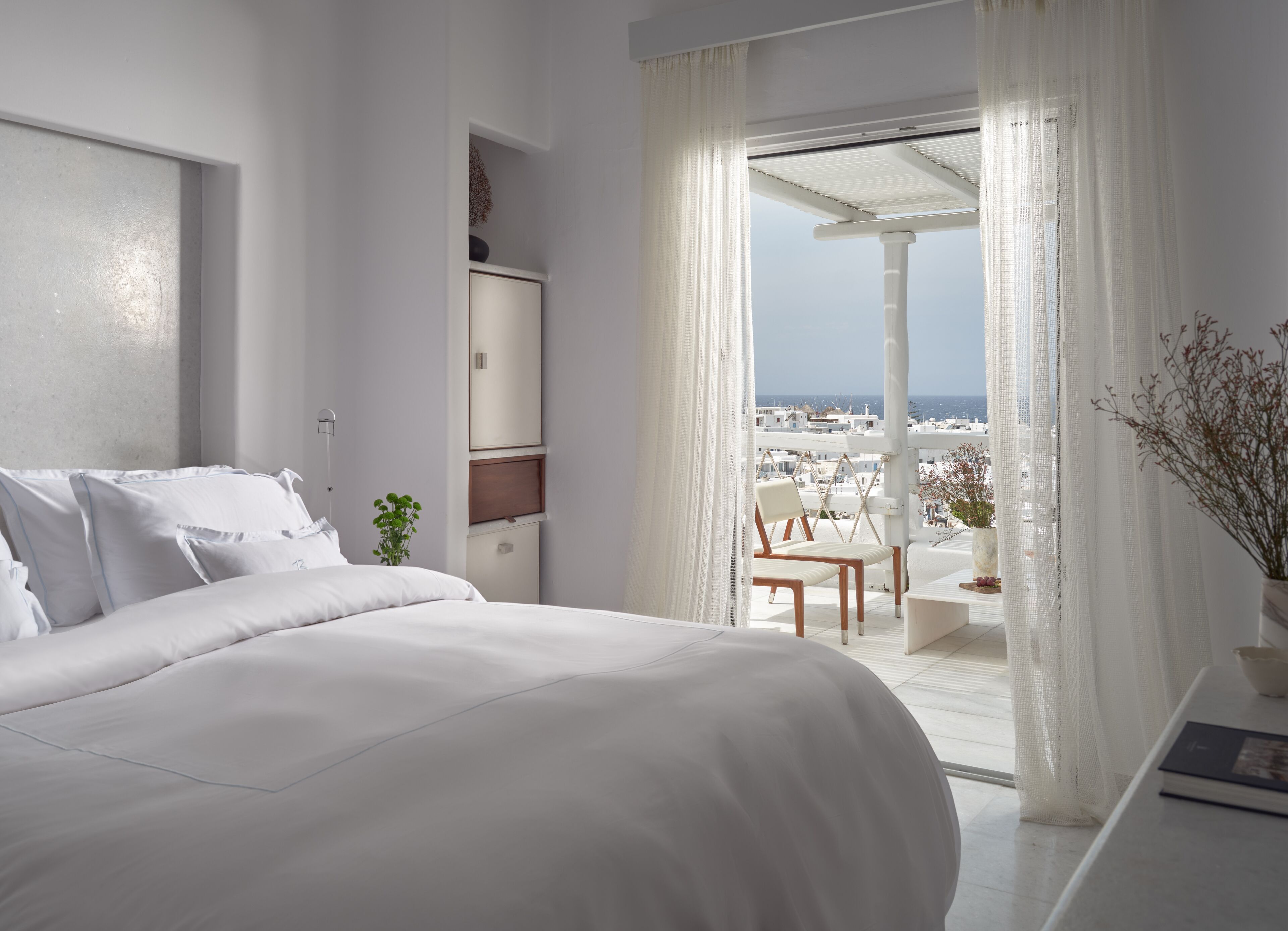 A modern hotel room with a large bed, a small seating area with a view of the city, and a balcony with a view of the sea.