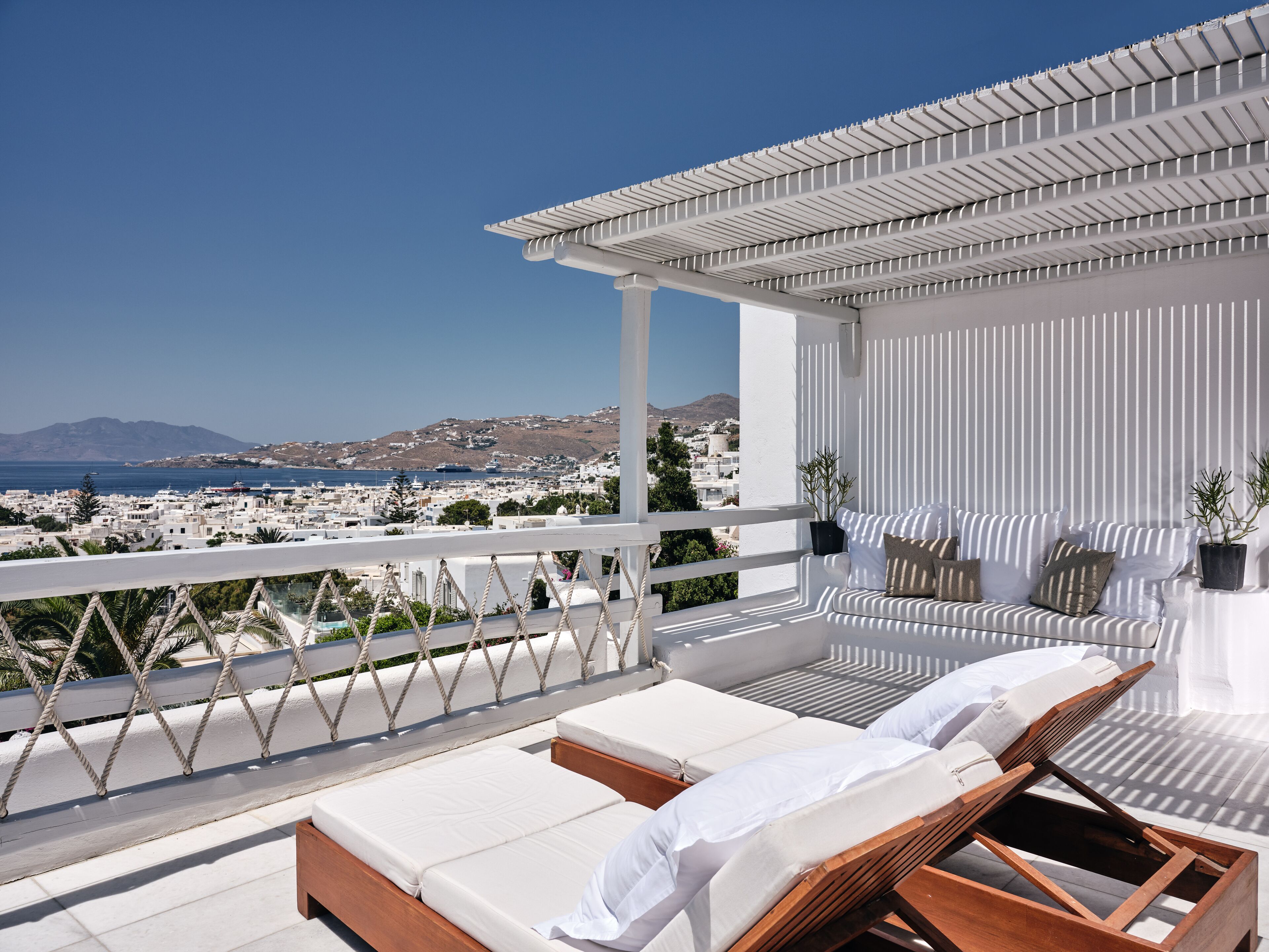 A balcony with two sun loungers, a pergola, and a view of a coastal town.
