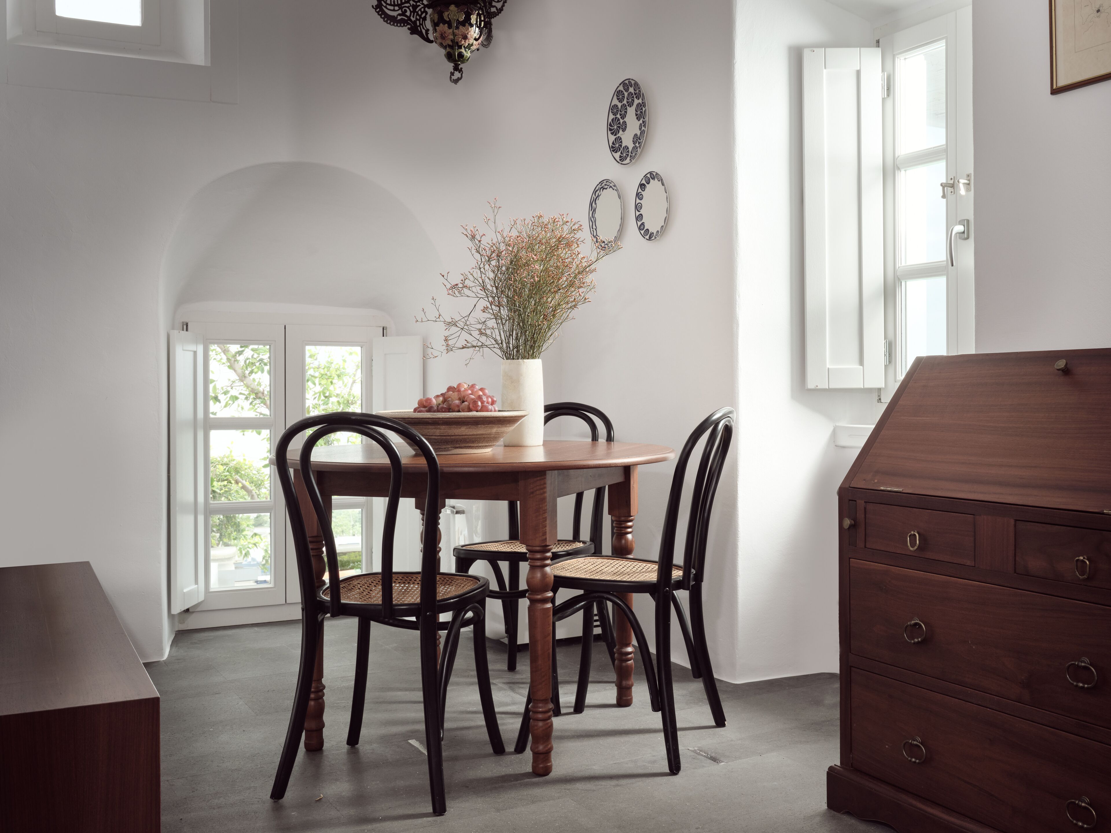 A dining area with a round table, four chairs, a vase with flowers, and wall decorations.