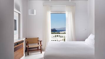 A bedroom with a large bed, a wooden chair, a dresser, and a window with a view of a ship and cityscape.