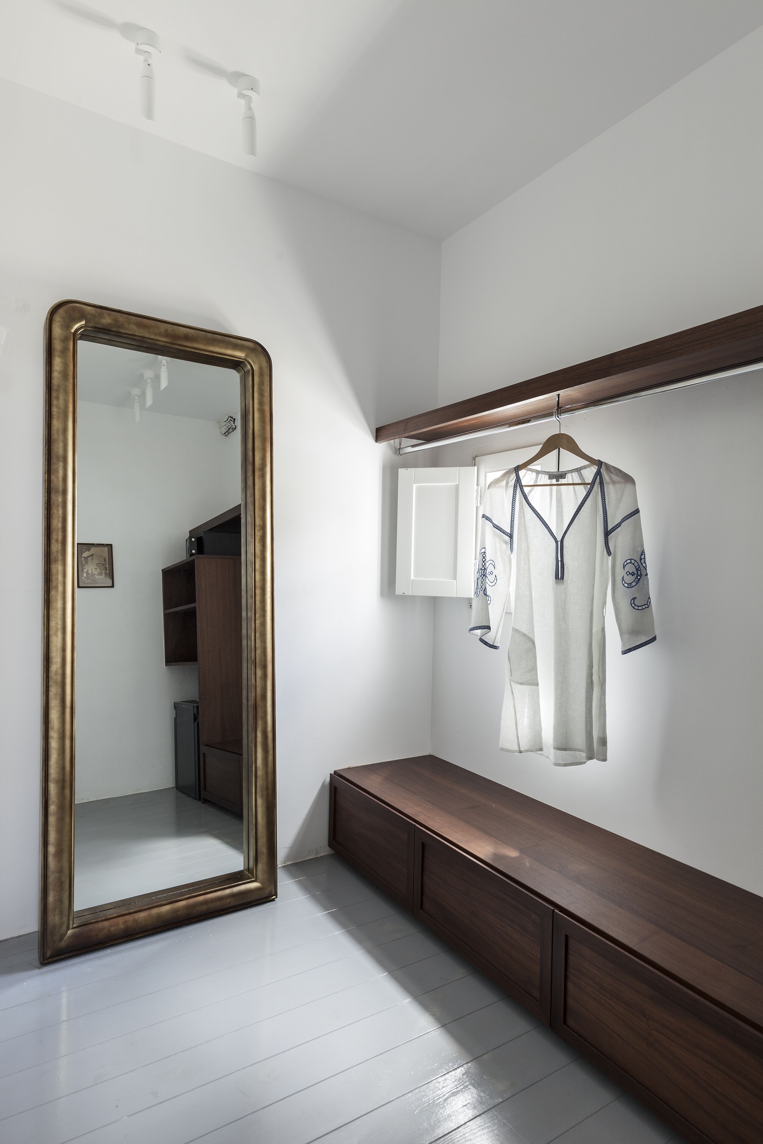 A room with a large mirror, a wooden bench, and a hanging garment.