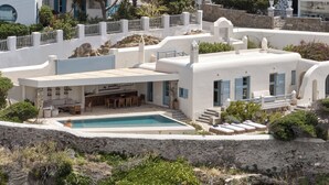 A white building with a pool, outdoor seating, and a stone wall. - Belvedere Hotel - The Leading Hotels of the World  (Mykonos)