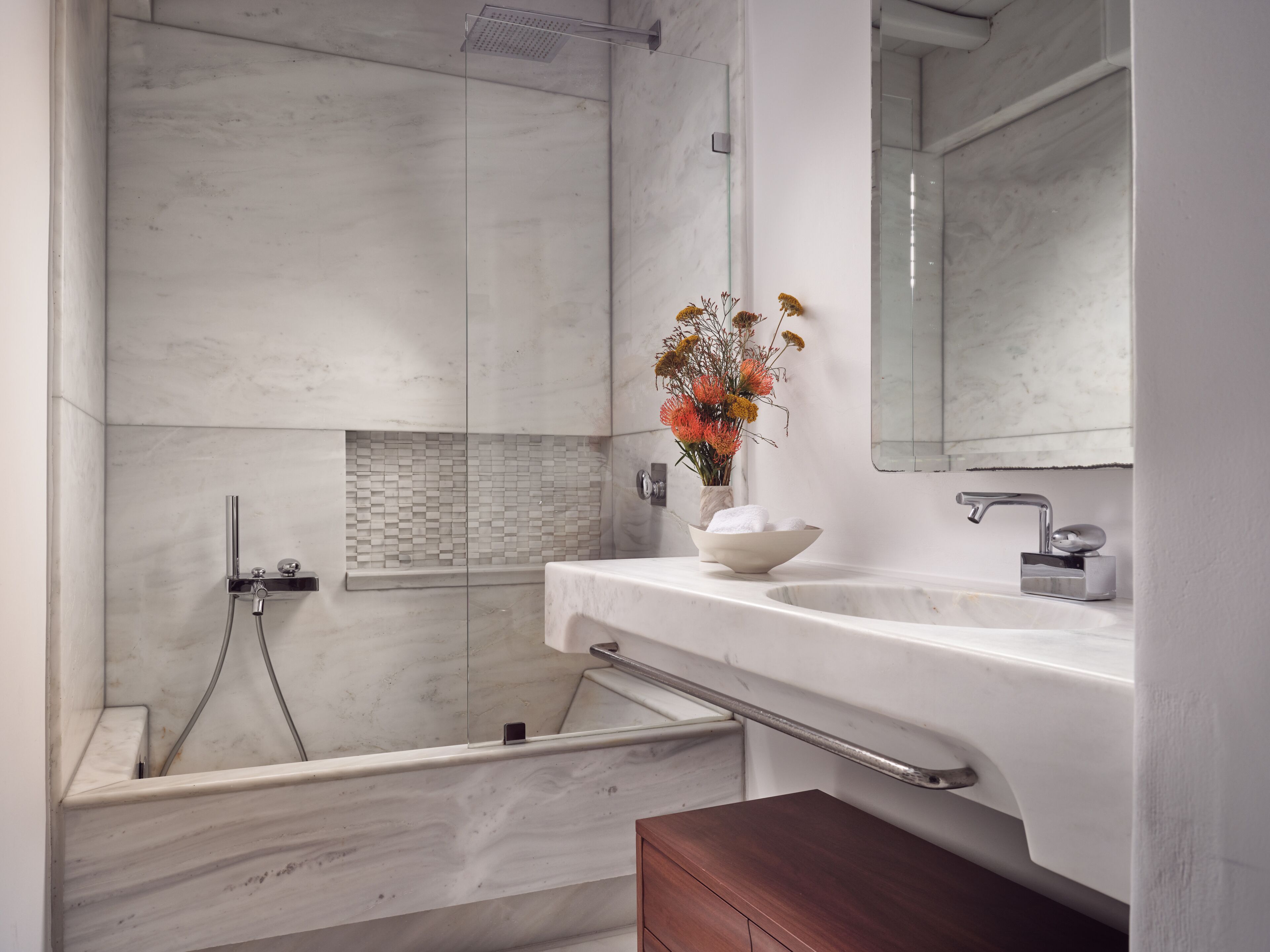 A modern bathroom with a marble sink, a glass shower enclosure, and a wooden vanity.