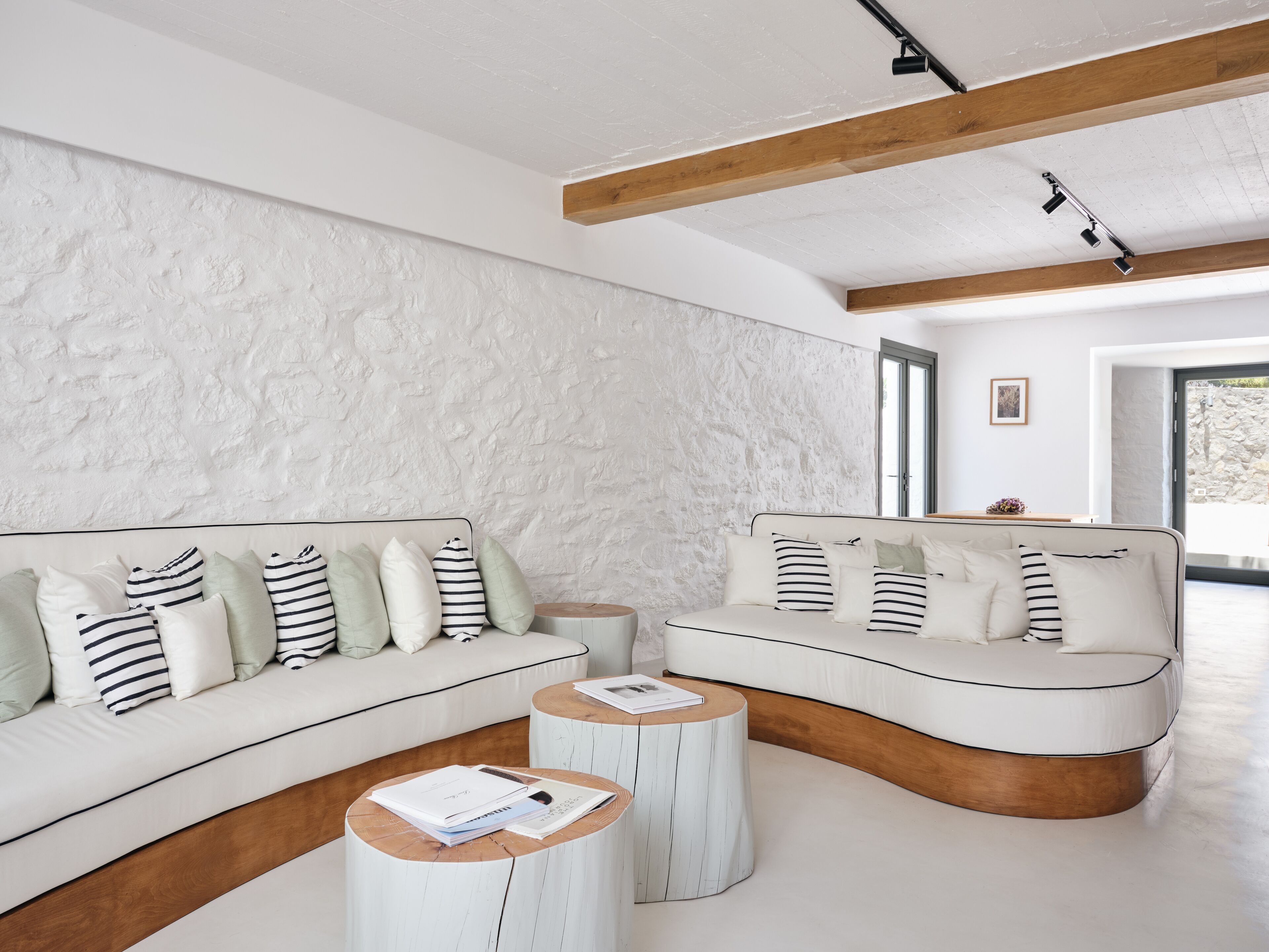 Una sala de estar moderna con una pared blanca texturizada, un sofá blanco con almohadones a rayas y una mesa de centro de madera con papeles.
