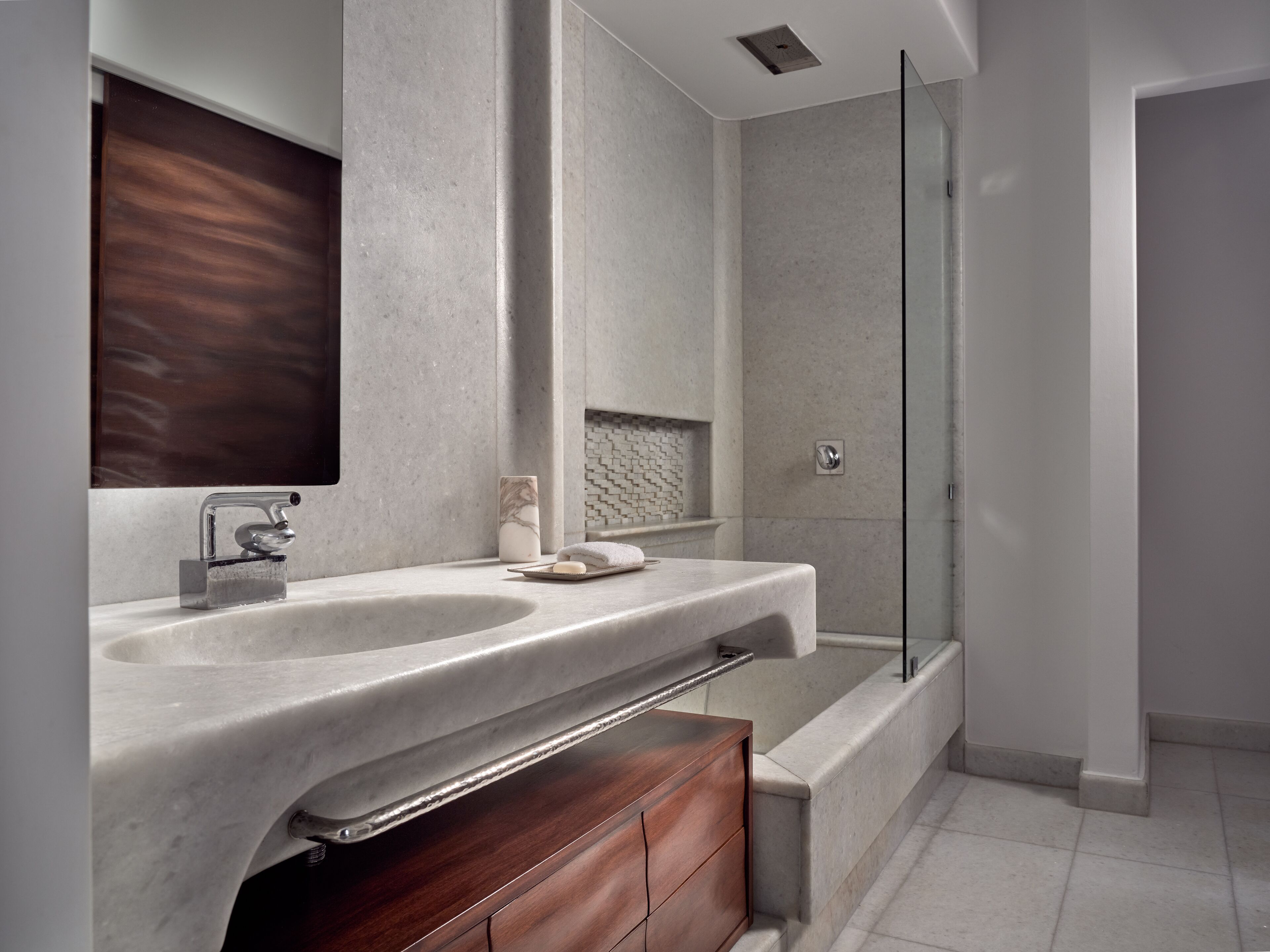 A modern bathroom with a large marble sink, a wooden vanity, a glass shower enclosure, and a tiled floor.