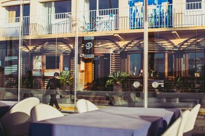 Un restaurant avec une terrasse, une enseigne indiquant qu’il s’agit d’un restaurant, et une personne qui passe.