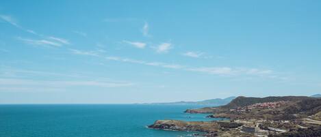 A coastal landscape with a clear sky, rocky terrain, and a distant view of a town with buildings.