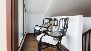 Een balkon met twee rieten stoelen, een tafeltje met een lantaarn, en uitzicht op de omgeving.