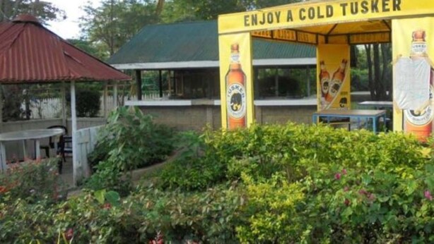 Un pabellón con un letrero que dice "ENJOY A COLD TUSKER" rodeado de follaje.
