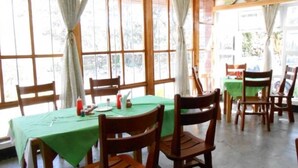 Un comedor con una mesa verde, sillas de madera y ventanas amplias.