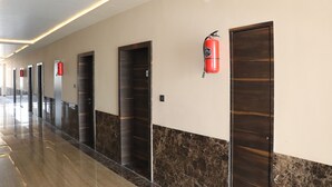 Un pasillo con varias puertas, un extintor de incendios sujeto a la pared y un suelo de mármol.