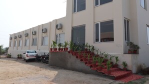 Un edificio de varios pisos con unidades de aire acondicionado, una escalera adornada con plantas en macetas y un coche estacionado.