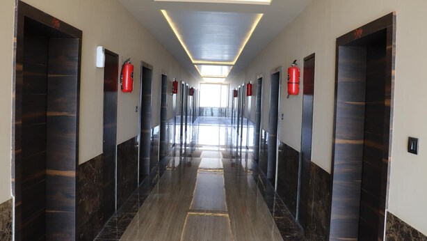 Un pasillo largo y bien iluminado con varias puertas, cada una con un extintor rojo montado encima.