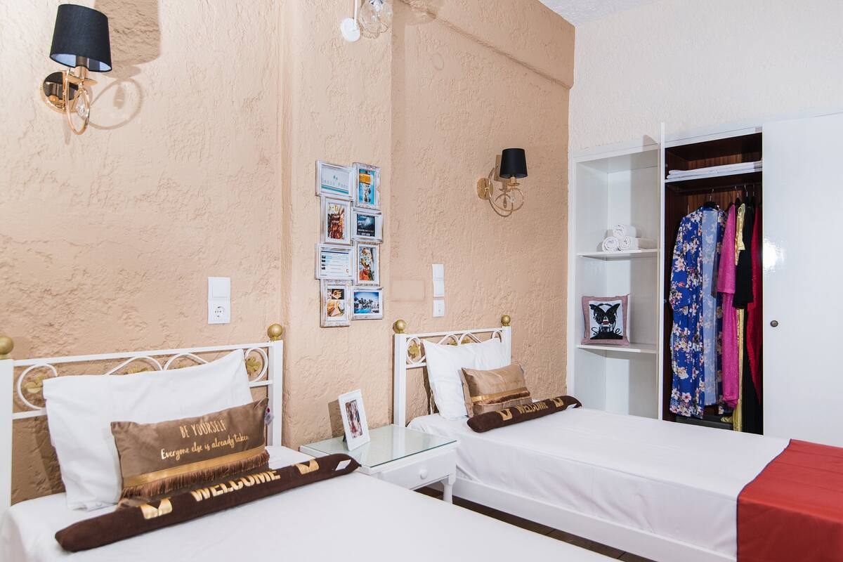 A bedroom with two beds, a wardrobe, a bedside table, and wall-mounted lamps.