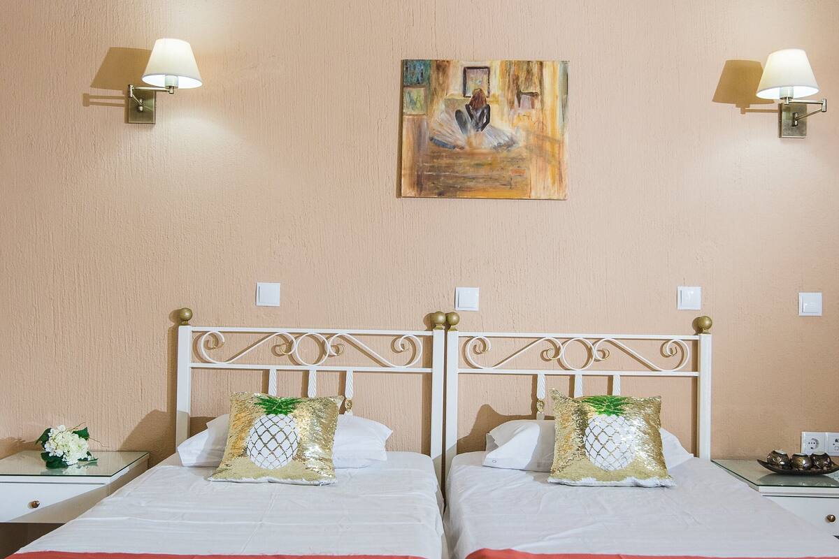 A hotel room with two beds, a painting on the wall, and an air conditioning unit above.