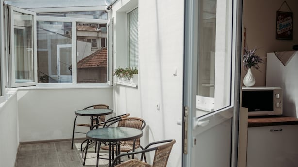 Un petit balcon avec une porte vitrée, une petite table avec des chaises, une plante en pot et un four à micro-ondes posé sur un comptoir.