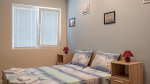 Une chambre à coucher avec un lit en bois, une table de chevet et une commode, ainsi qu’une fenêtre avec des stores.