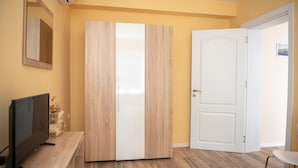 Une pièce avec un plancher en bois, une armoire blanche, un téléviseur et une porte.
