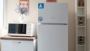 Une petite cuisine équipée, comprenant un micro-ondes posé sur un mini-réfrigérateur, un petit placard et une étagère avec des objets décoratifs.