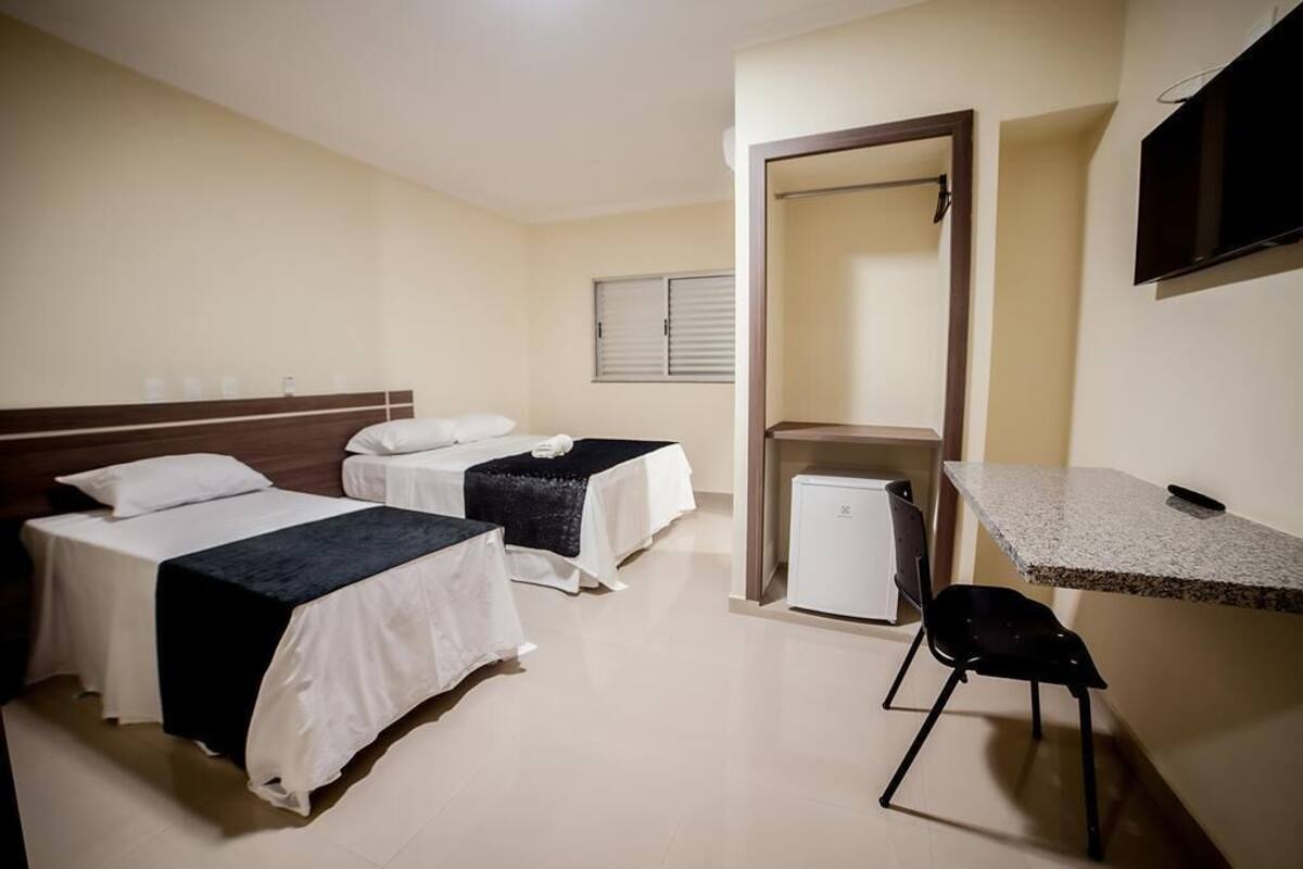 A hotel room with two beds, a desk, a chair, a television, and a small refrigerator.